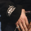 Close-up of a hand wearing a silver bracelet with white beads on a dark background