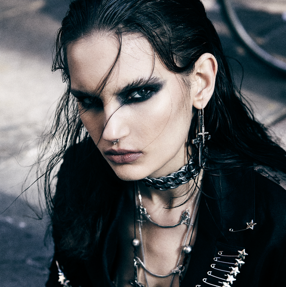 Woman with dark hair and makeup wearing a black outfit with metallic details.