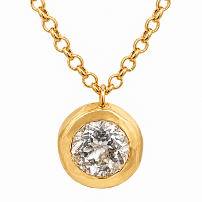 A gold pendant necklace featuring a round bezel-set clear gemstone on a delicate gold chain, shown against a plain white background.