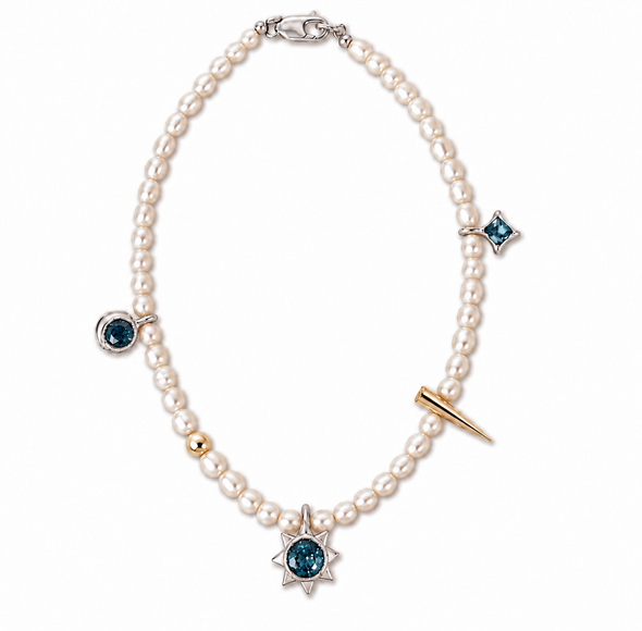 A pearl beaded necklace with silver-toned star and moon charms, one of which features a round blue gemstone. The necklace also includes a small gold bead, a gold-toned spike charm, and a small blue gemstone moon charm, all displayed on a clean white background.