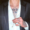 Person wearing a suit with visible tattoos on neck and arms, holding a cigarette.