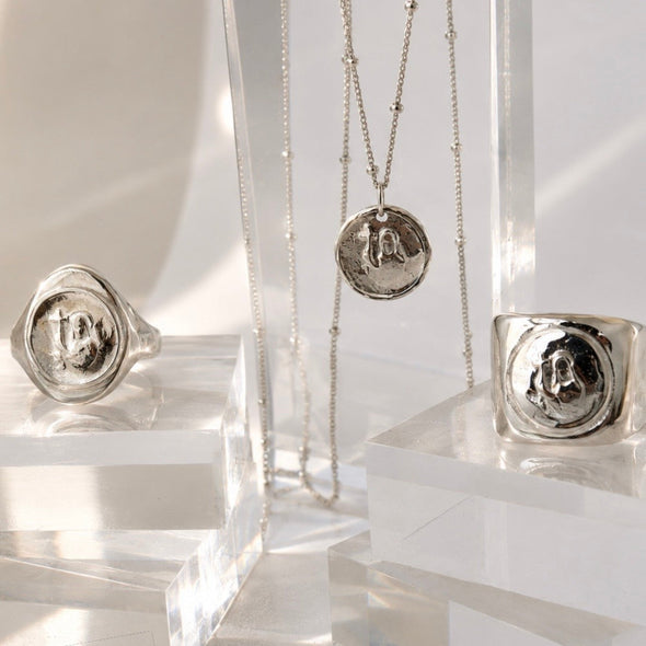 Silver jewelry including rings and a necklace on clear stands against a white background