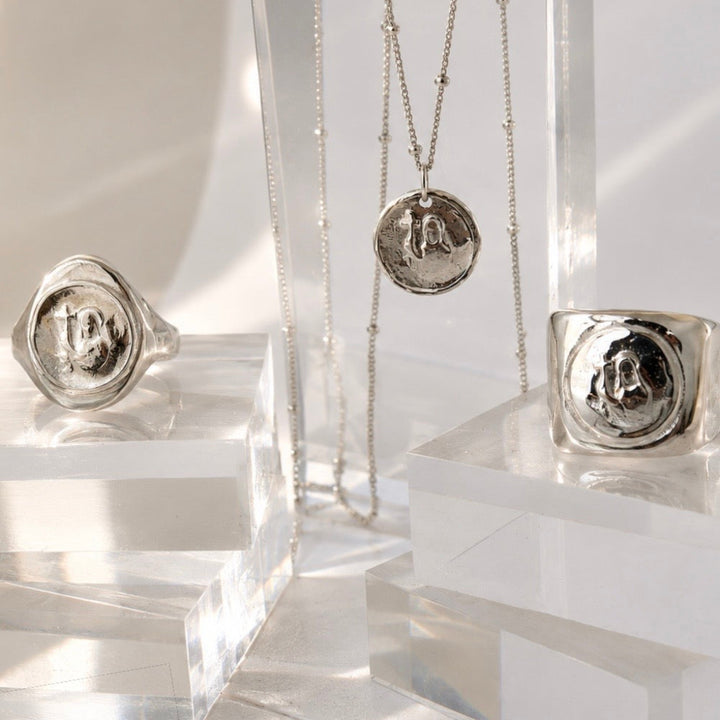 Silver jewelry including rings and a necklace on clear stands against a white background