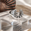 Silver horseshoe-shaped ring with embedded stones on a reflective surface