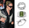 Person wearing a black leather jacket with fringe details, surrounded by silver rings with green gemstones.