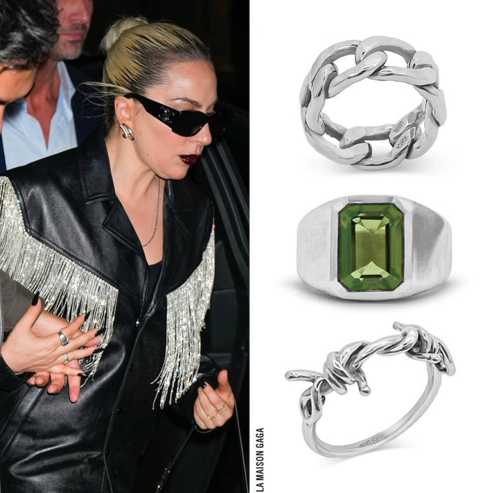 Person wearing a black leather jacket with fringe details, surrounded by silver rings with green gemstones.