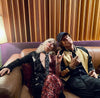 Two people sitting on a couch in a room with striped curtains.