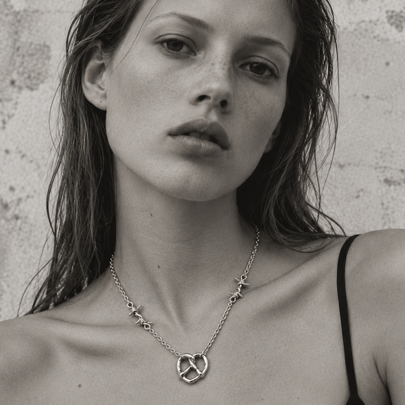 A close-up black and white portrait of a woman wearing a delicate chain necklace with a peace sign pendant and small star details, set against a textured wall.