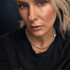 A close-up portrait of a woman with blonde hair wearing a black t-shirt with 'MOTLEY CRÜE' printed in red across the chest, and a silver chain necklace.