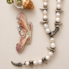 Pearl necklace with seashells and a small shell with green gemstones on a beige background