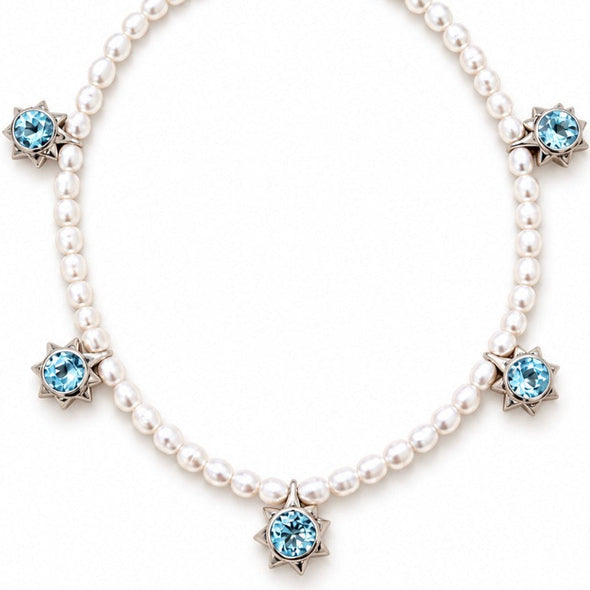 A pearl necklace with five light blue faceted gemstones set in silver starburst clusters, arranged in a circle on a white background.