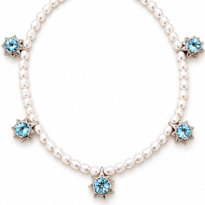 A pearl necklace with five light blue faceted gemstones set in silver starburst clusters, arranged in a circle on a white background.