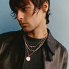 Man wearing a black leather jacket and layered necklaces against a light blue background