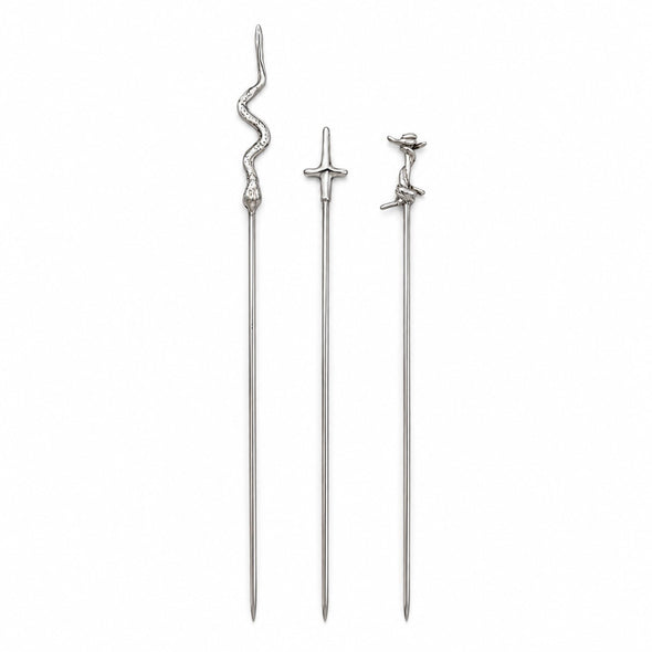 Three silver-toned metal cocktail picks with decorative tops, including a snake, a sword, and a small figure, shown on a plain white background.