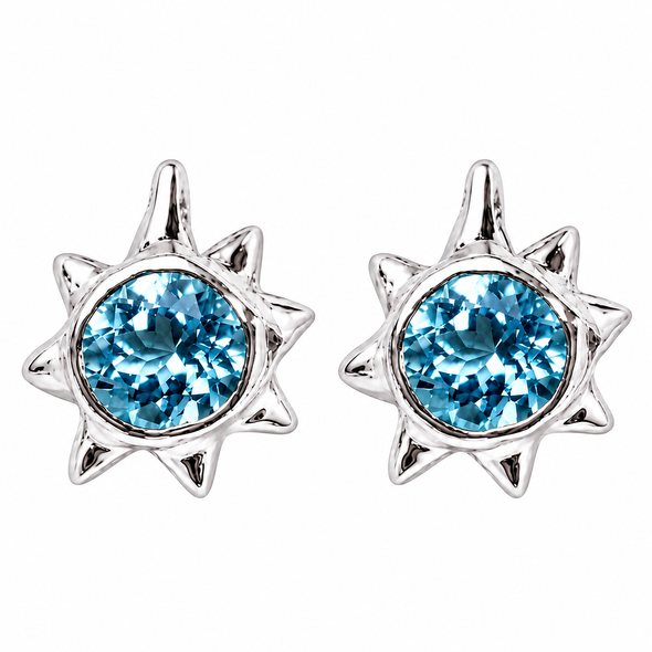 A pair of silver starburst stud earrings featuring round, faceted light blue gemstones in the center, set against a plain white background.