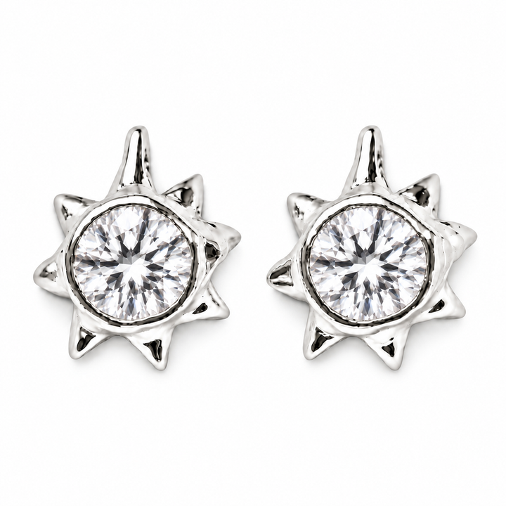 A pair of silver starburst stud earrings with round clear gemstones, shown on a plain white background.