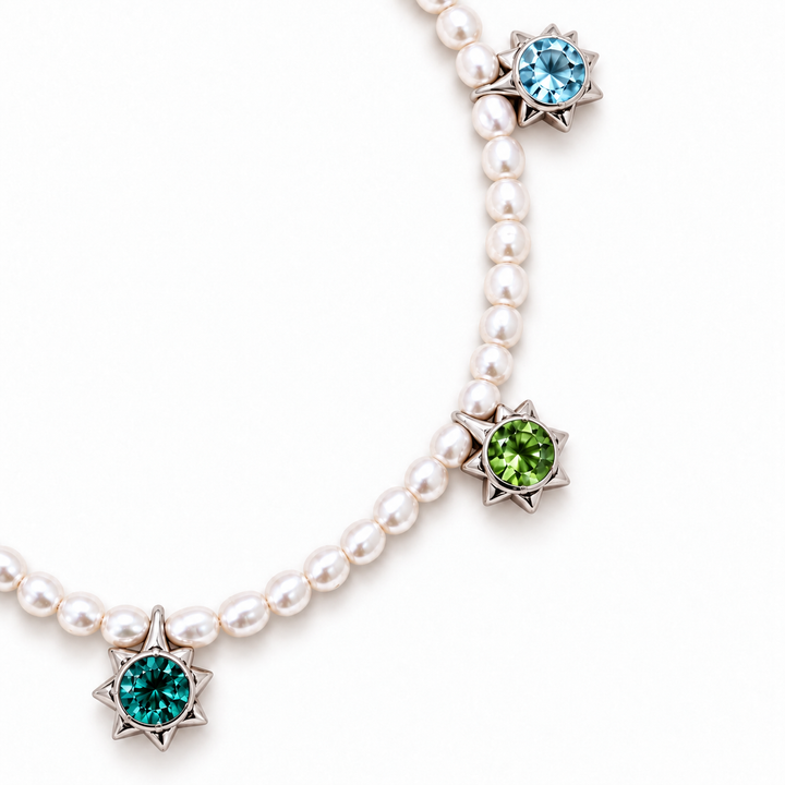 A pearl necklace with three star-shaped silver pendants, each set with a round gemstone in a different color: light blue, green, and teal, on a white background.