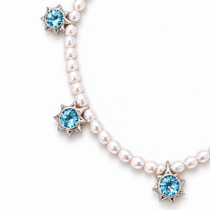 A pearl necklace with silver starburst charms, each featuring a round light blue gemstone, shown on a clean white background.