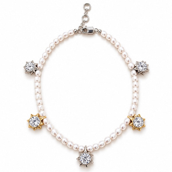 A pearl charm bracelet with silver and gold starburst settings holding clear gemstones, displayed on a clean white background.