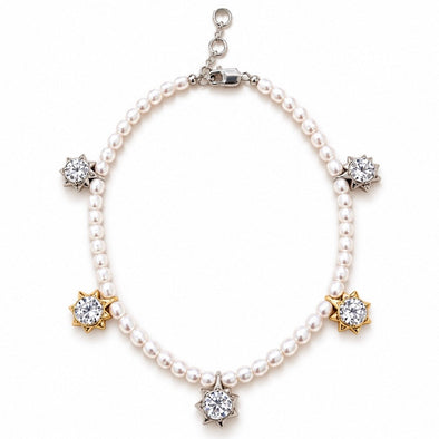 A pearl charm bracelet with silver and gold starburst settings holding clear gemstones, displayed on a clean white background.