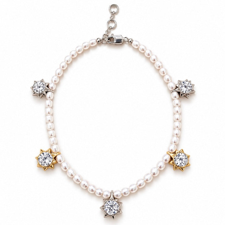 A pearl charm bracelet with silver and gold starburst settings holding clear gemstones, displayed on a clean white background.