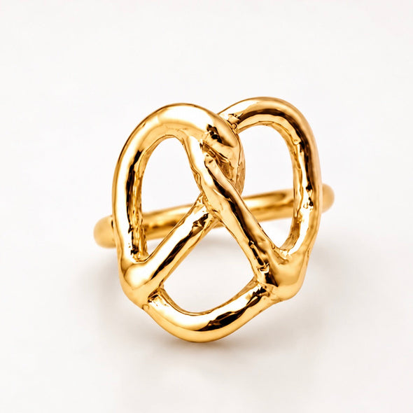 A gold ring designed in the shape of a pretzel, featuring a polished, textured finish on a clean white background.