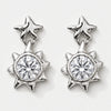 A pair of silver-toned dangle earrings featuring a star-shaped post with a dangling spiky sunburst pendant, each set with a clear round-cut gemstone, shown on a light gray background.
