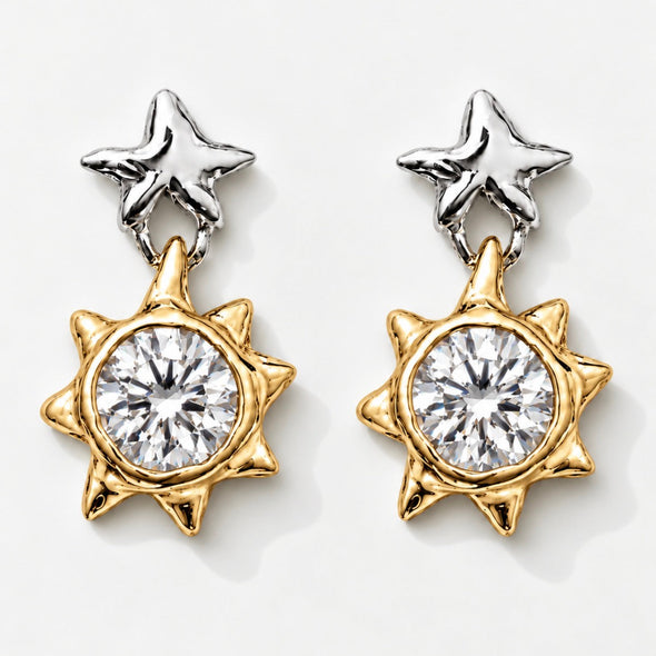 A pair of two-tone star and sun dangle earrings. Each earring features a polished silver star stud at the top and a gold-toned sunburst charm with a large clear round-cut center stone, set against a clean white background.