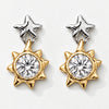 A pair of two-tone star and sun dangle earrings. Each earring features a polished silver star stud at the top and a gold-toned sunburst charm with a large clear round-cut center stone, set against a clean white background.