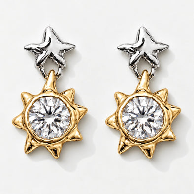 A pair of two-tone star and sun dangle earrings. Each earring features a polished silver star stud at the top and a gold-toned sunburst charm with a large clear round-cut center stone, set against a clean white background.