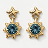 A pair of gold dangle earrings featuring a star-shaped top and a sunburst lower section with a faceted blue gemstone, shown on a clean white background.