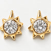 A pair of gold starburst stud earrings with a large round clear gemstone in the center, set against a plain white background.