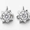 A pair of silver-toned starburst stud earrings with a clear round-cut gemstone in the center, set against a plain light gray background.