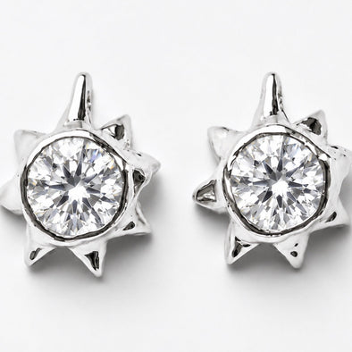 A pair of silver-toned starburst stud earrings with a clear round-cut gemstone in the center, set against a plain light gray background.
