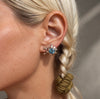 A close-up of a model's ear wearing a silver star-shaped stud earring with a central light blue gemstone and small silver beads on the lobe.