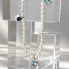 A pearl beaded necklace with silver-toned settings and blue gemstones, displayed on clear acrylic blocks against a light gray background.