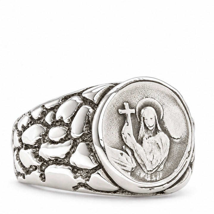 A silver signet ring featuring a circular medallion with an embossed figure holding a cross, set against a textured, stone-like band on a clean white background.