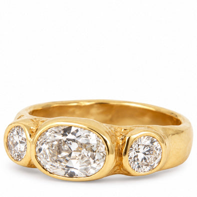 A yellow gold ring featuring a large oval-cut diamond center stone flanked by two smaller round-cut diamonds in a three-stone setting, shown on a plain white background.
