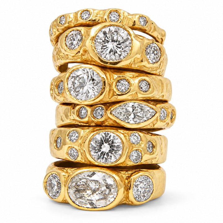 A stack of five textured yellow gold rings, each featuring a large round brilliant-cut diamond and smaller accent diamonds, set against a plain white background.