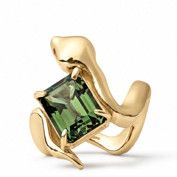 A gold ring sculpted in the shape of a frog, featuring a large green emerald-cut gemstone on a clean white background.