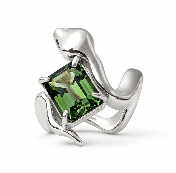 A silver ring featuring a large, faceted green rectangular gemstone held by sculptural, flowing silver bands, photographed on a clean white background.