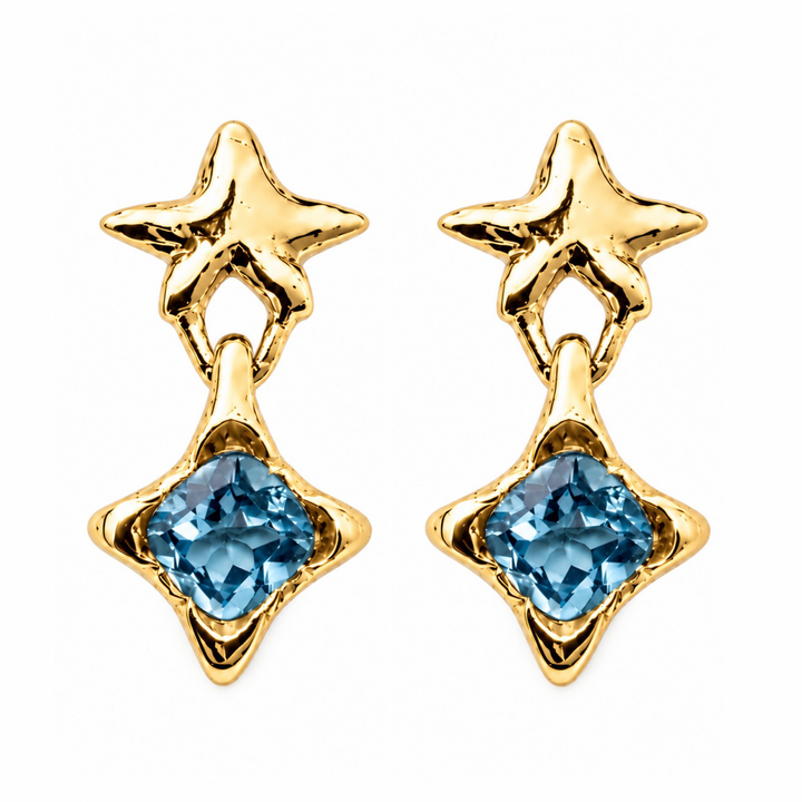 A pair of gold star-shaped drop earrings with a faceted light blue gemstone at the bottom, shown on a plain white background.