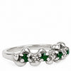 A silver flower-shaped ring featuring green emerald-cut gemstones and small clear accent stones, shown on a plain white background.