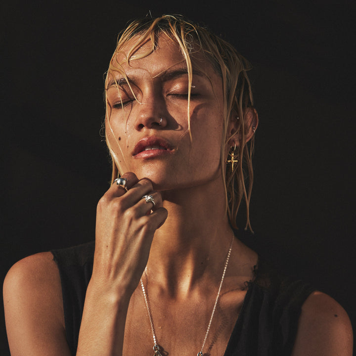 Woman with wet hair and minimal makeup wearing jewelry against a dark background