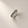 A silver band ring featuring a row of green faceted gemstones, photographed on a clean, light beige background.