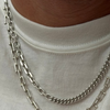 A close-up of a person wearing a layered silver chain necklace over a white crew-neck t-shirt.