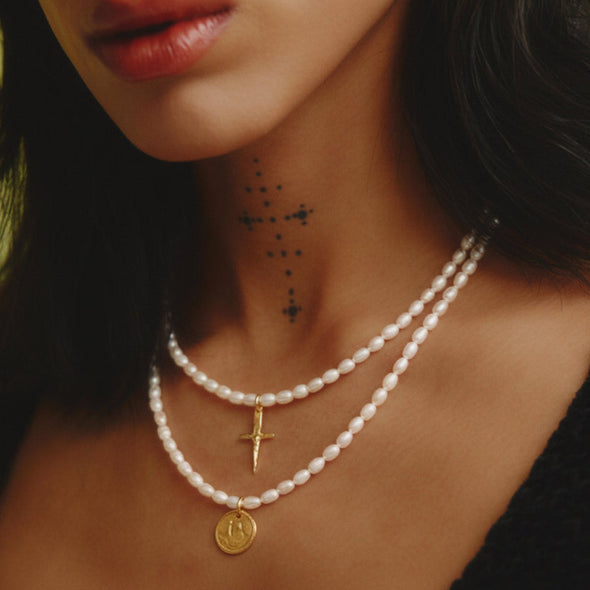 Close-up of a woman wearing a pearl necklace and earrings with a green background