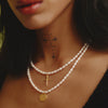 Close-up of a woman wearing a pearl necklace and earrings with a green background