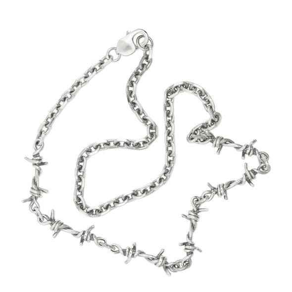 A silver necklace featuring a barbed wire link design with asymmetrically placed pendants on a cable chain.