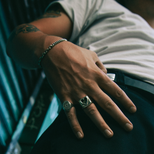 Close-up of a person's hand with rings and a bracelet, wearing a gray shirt.